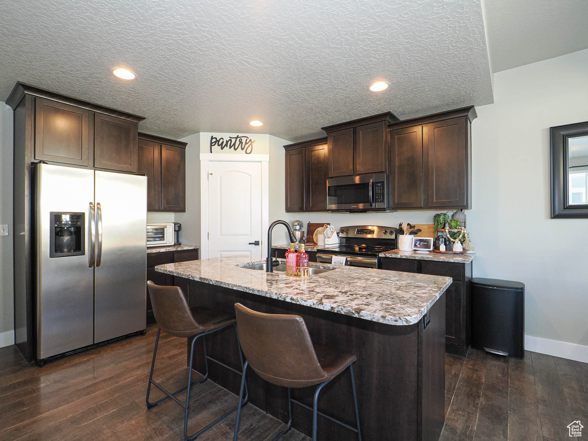 Kitchen featuring dark brown cabinetry, sink, dark hardwood / wood-style floors, an island with sink, and appliances with stainless steel finishes