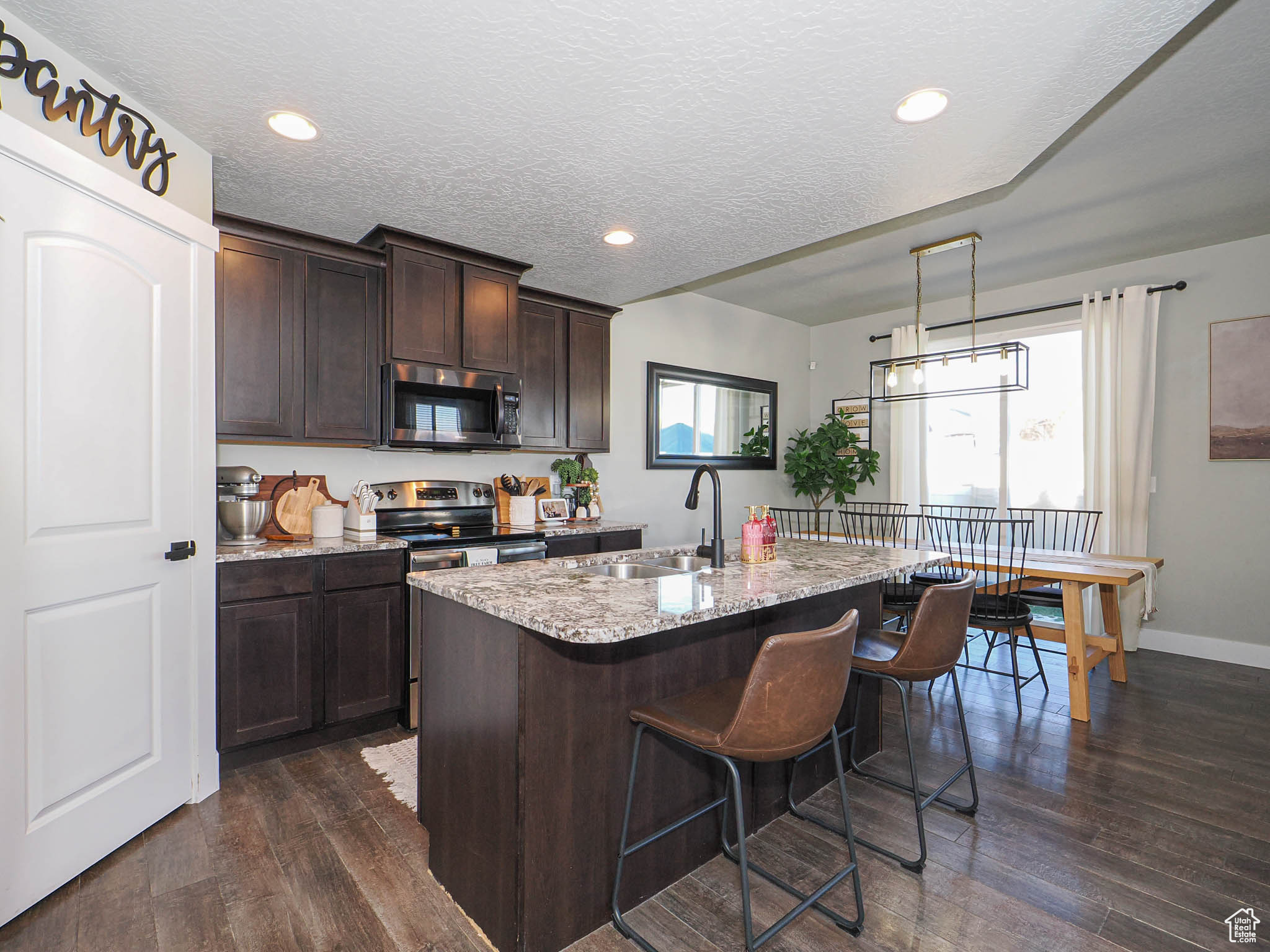 Kitchen with dark wood-type flooring, sink, a textured ceiling, an island with sink, and appliances with stainless steel finishes