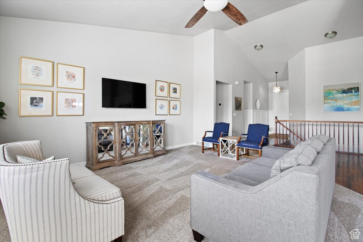 Living room with ceiling fan, carpet floors, and high vaulted ceiling