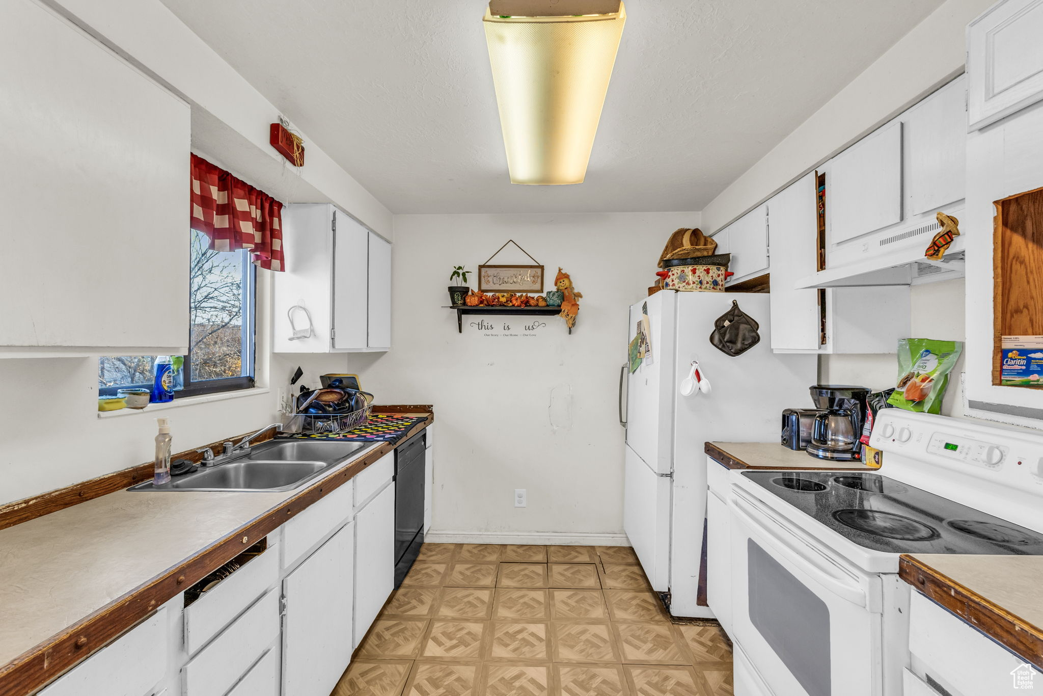 Kitchen with electric stove, white cabinetry, sink, and range hood