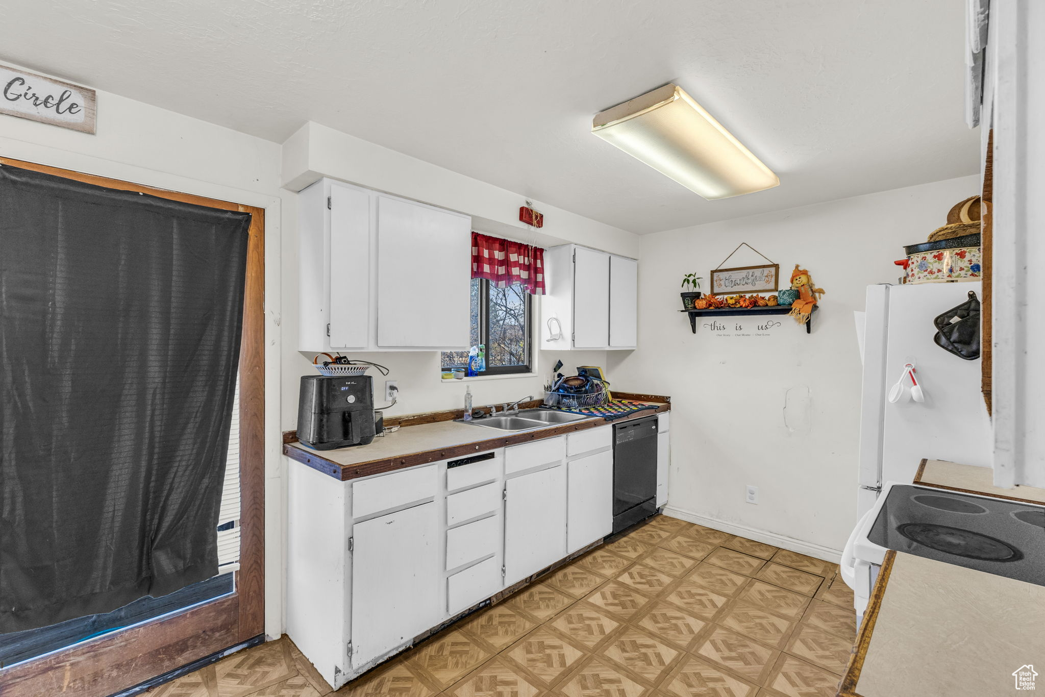 Kitchen with stove, sink, white cabinets, black dishwasher, and white fridge