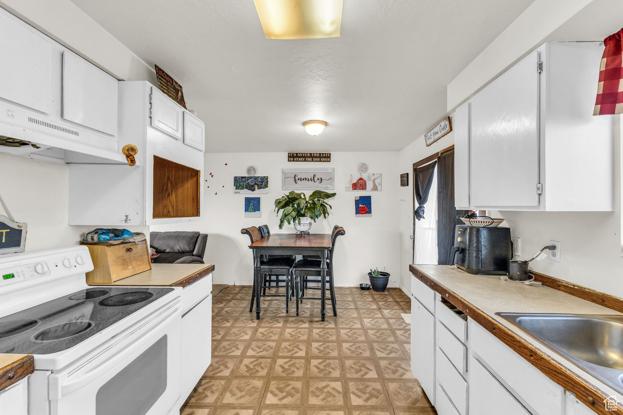 Kitchen featuring white electric range oven, ventilation hood, white cabinets, and sink