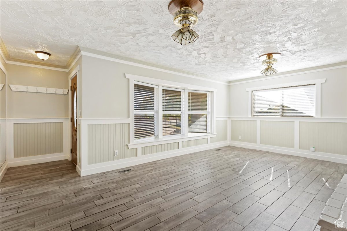 Unfurnished dining area with hardwood / wood-style floors, a textured ceiling, and ornamental molding