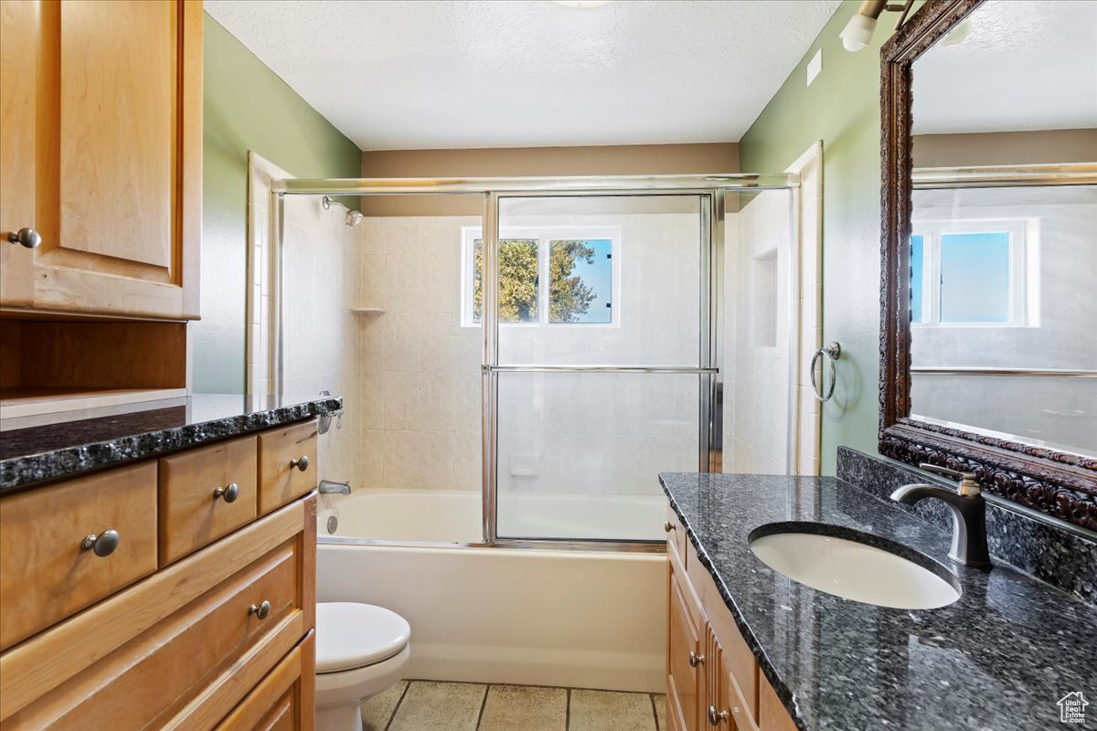 Full bathroom with tile patterned floors, a textured ceiling, combined bath / shower with glass door, toilet, and vanity