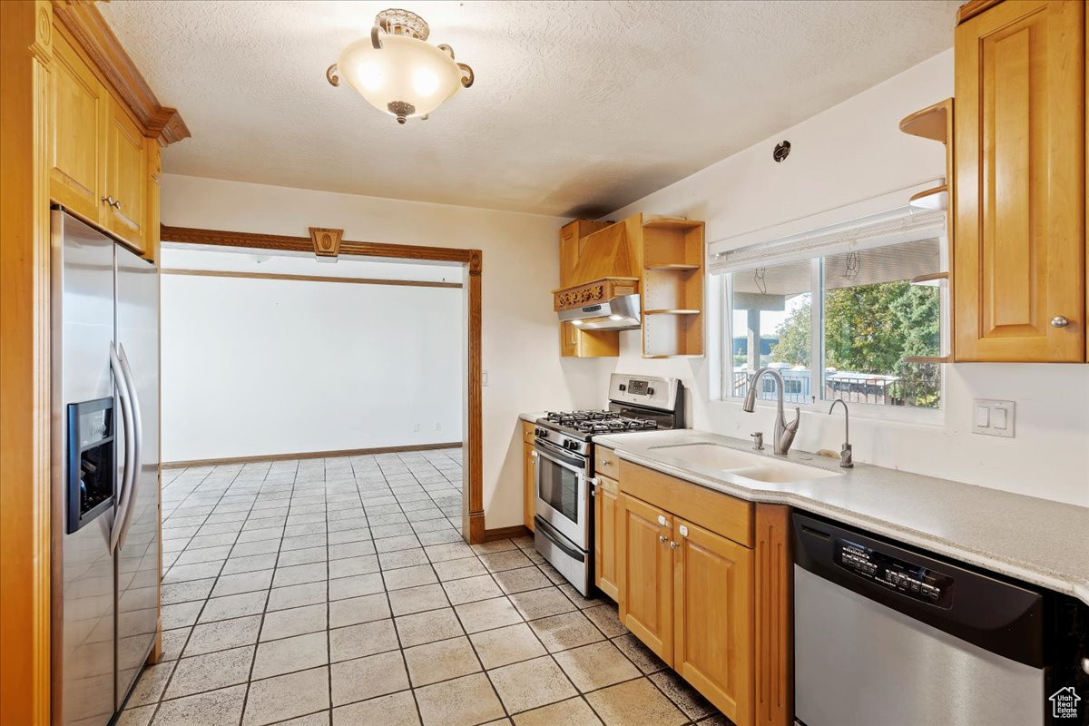 Kitchen with ventilation hood, sink, a textured ceiling, light tile patterned flooring, and stainless steel appliances