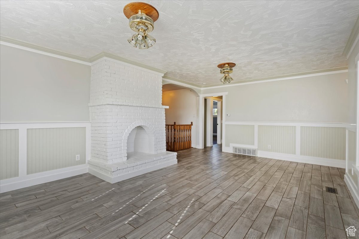 Unfurnished living room featuring a fireplace, wood-type flooring, a textured ceiling, and ornamental molding