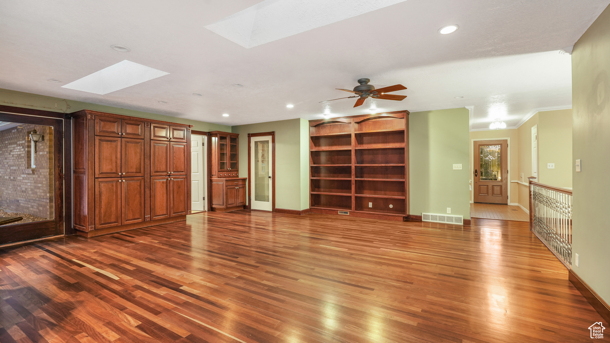 Unfurnished living room with dark hardwood / wood-style floors, ceiling fan, ornamental molding, and a skylight