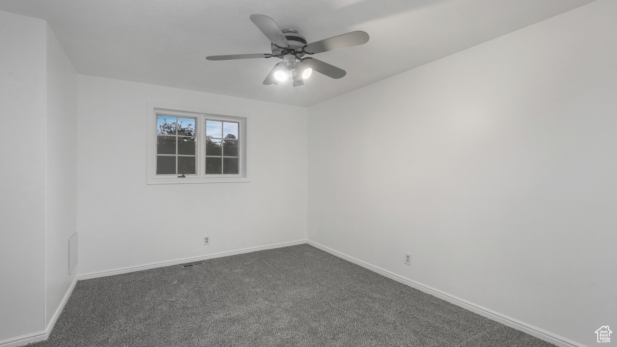 Empty room with ceiling fan and dark carpet