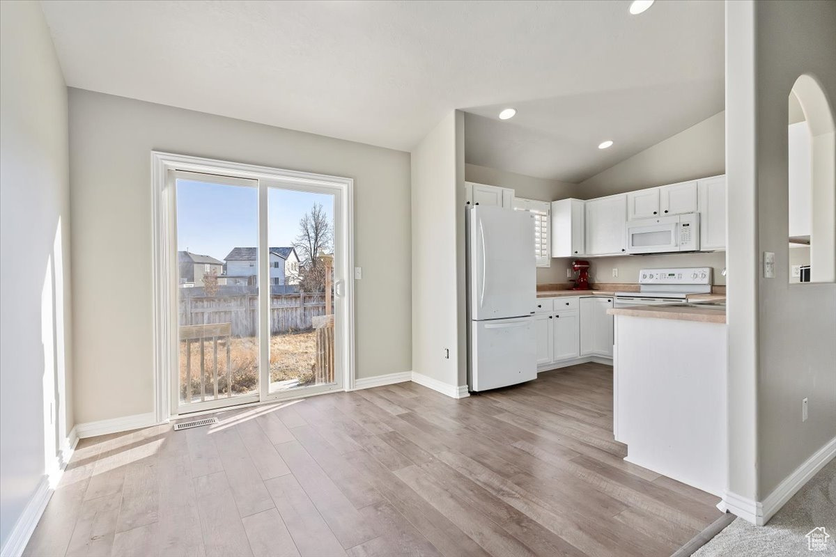 Kitchen with lofted ceiling, white cabinets, white appliances, and light wood-type flooring