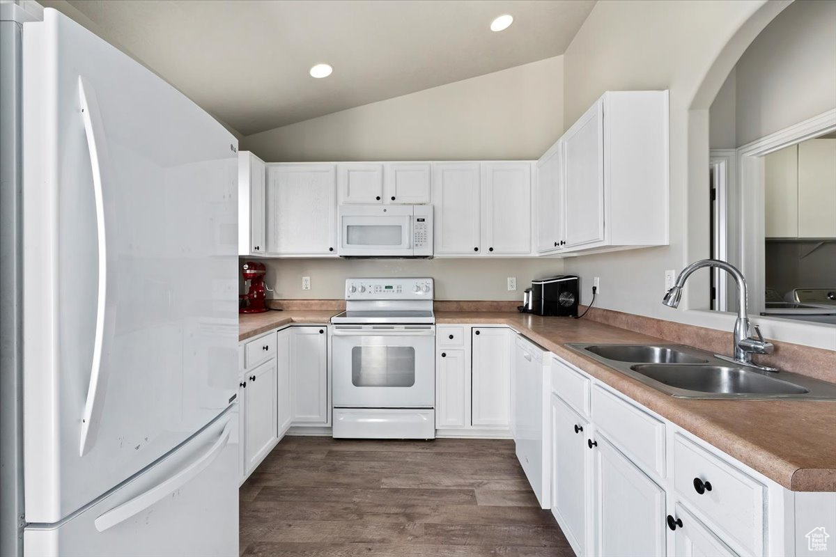 Kitchen featuring white appliances, white cabinetry, vaulted ceiling, and sink