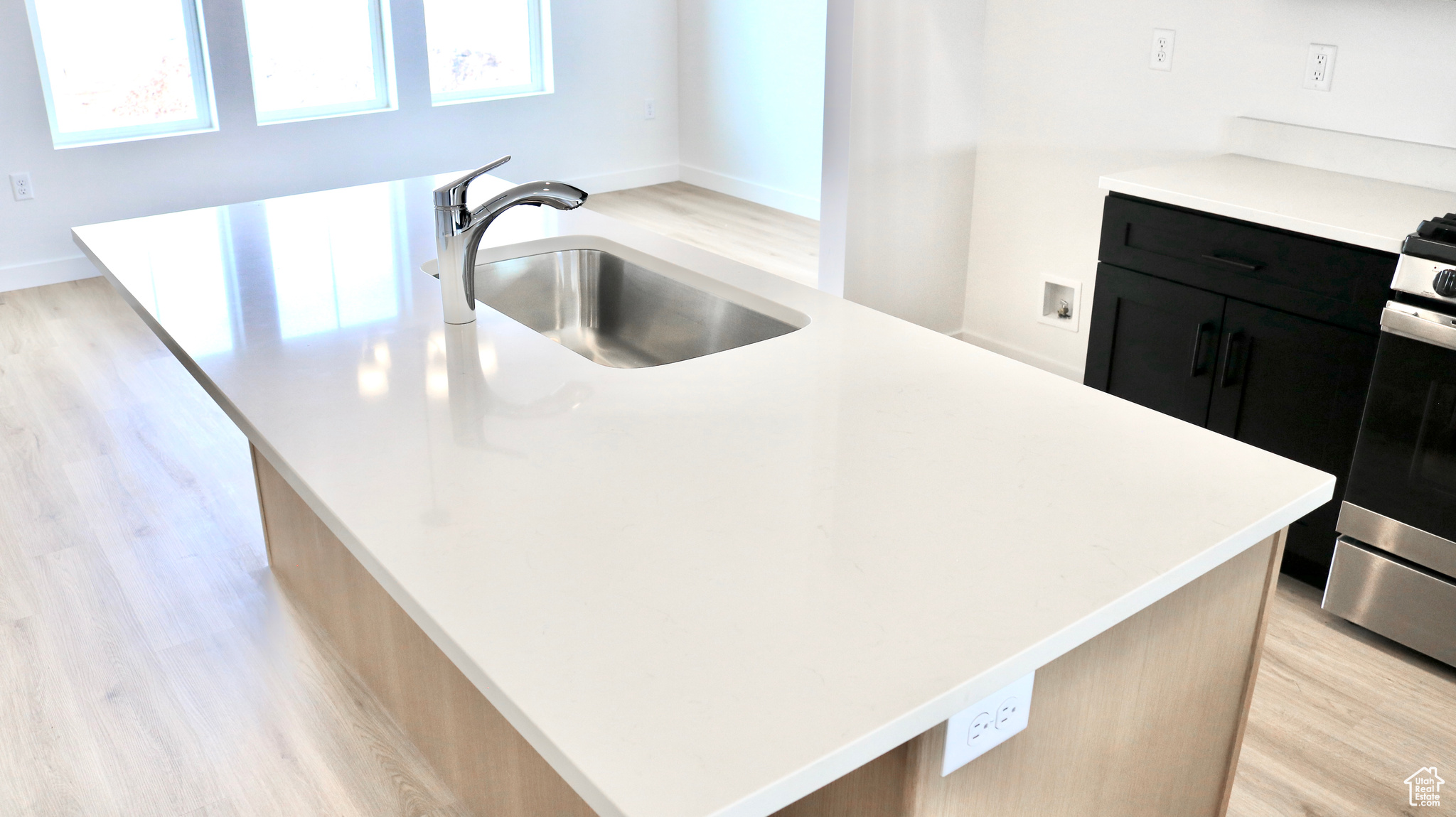 Kitchen with light wood-type flooring, a center island, stainless steel stove, and sink