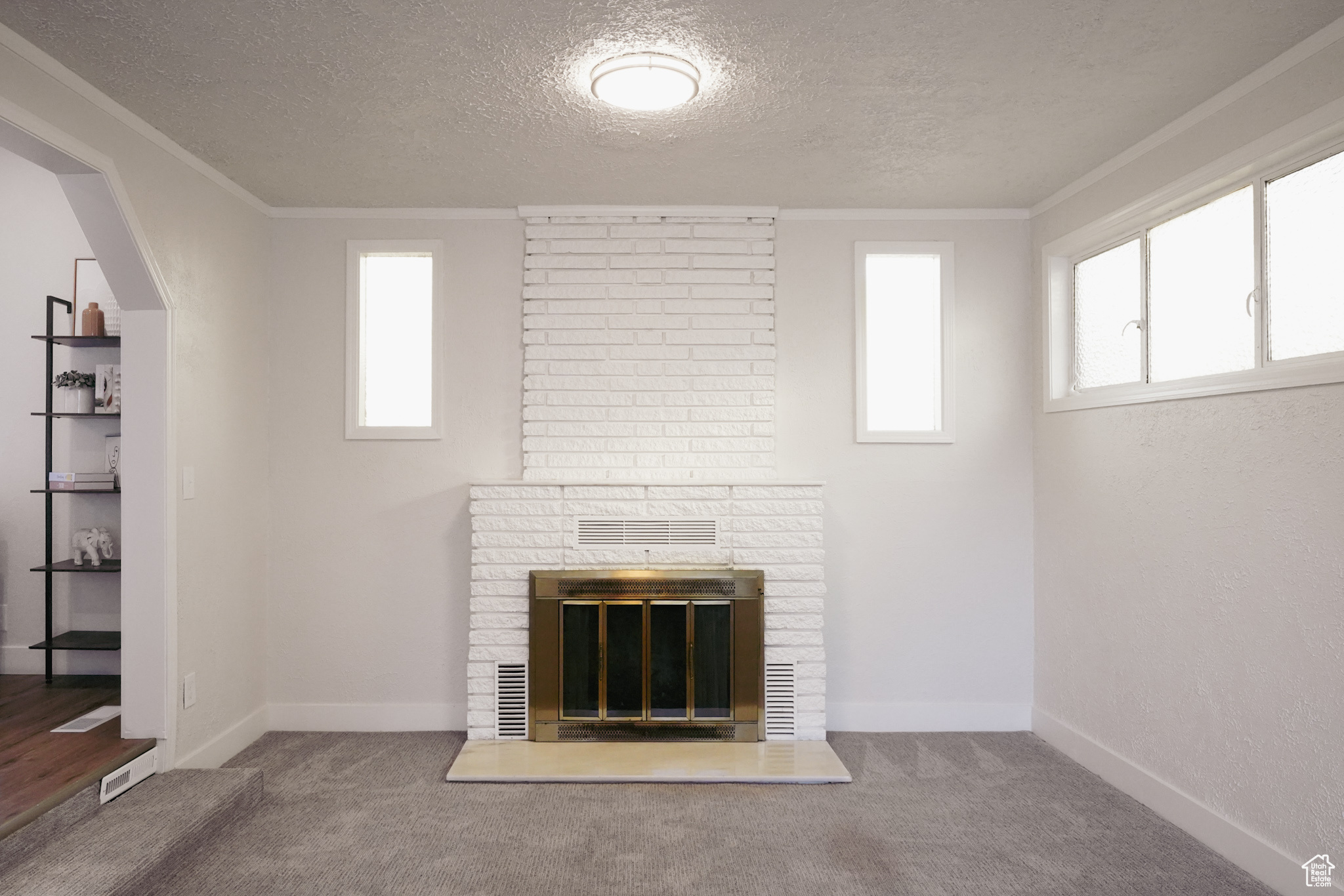 Interior details featuring carpet flooring, crown molding, a textured ceiling, and a brick fireplace