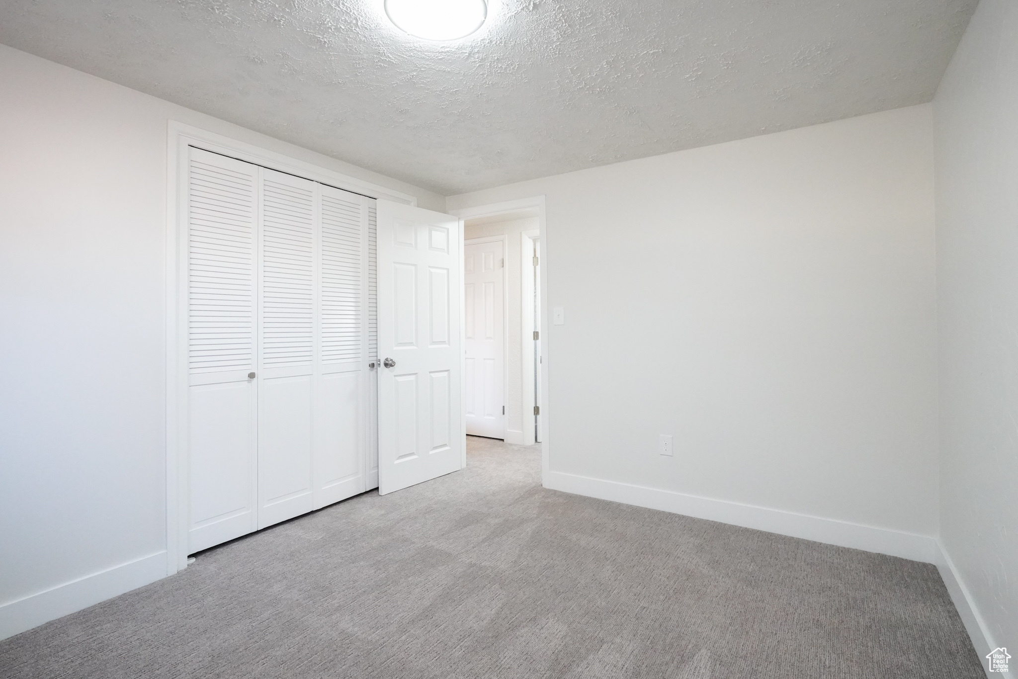 Unfurnished bedroom with light carpet, a closet, and a textured ceiling