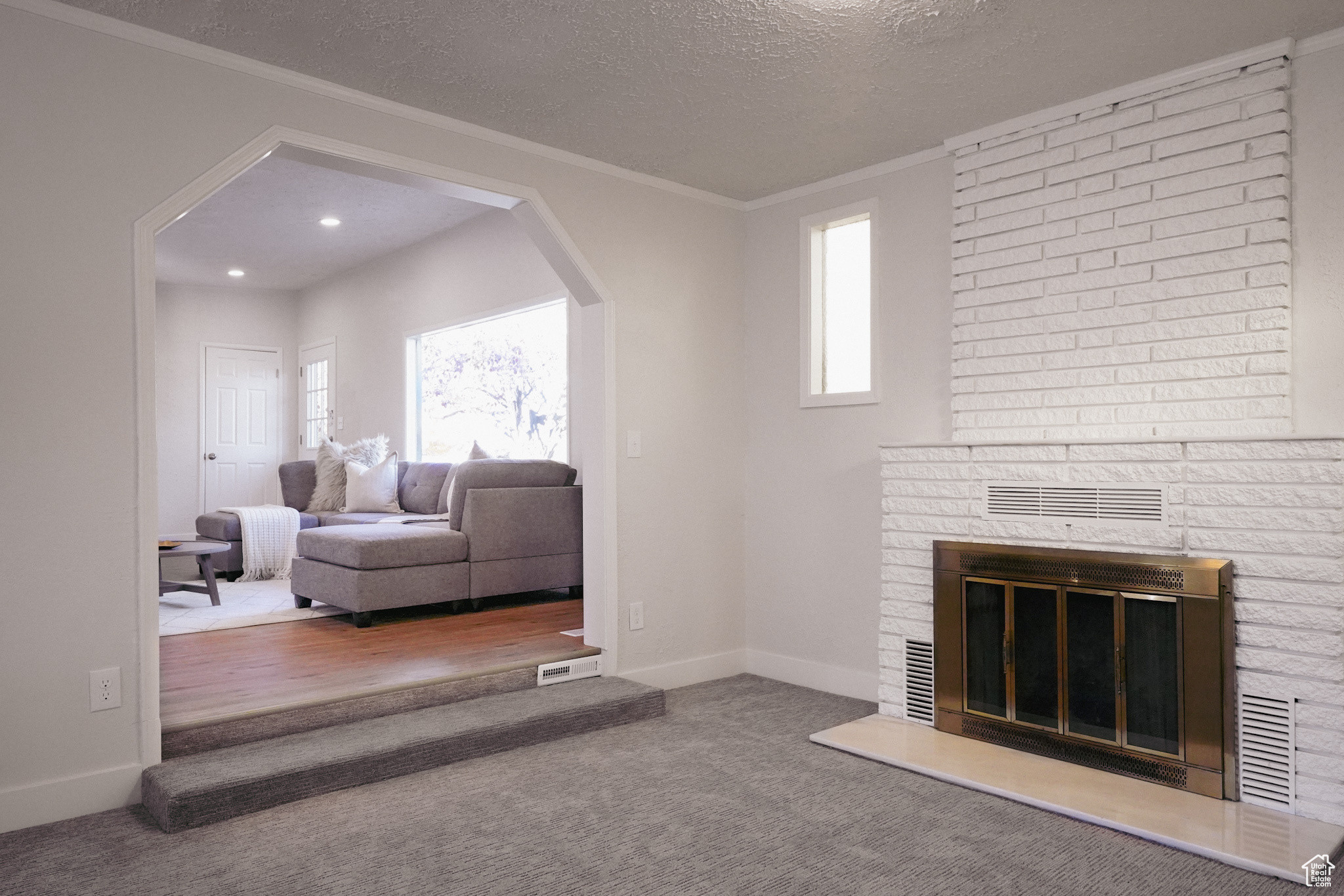 Living room featuring carpet, crown molding, a textured ceiling, and a brick fireplace