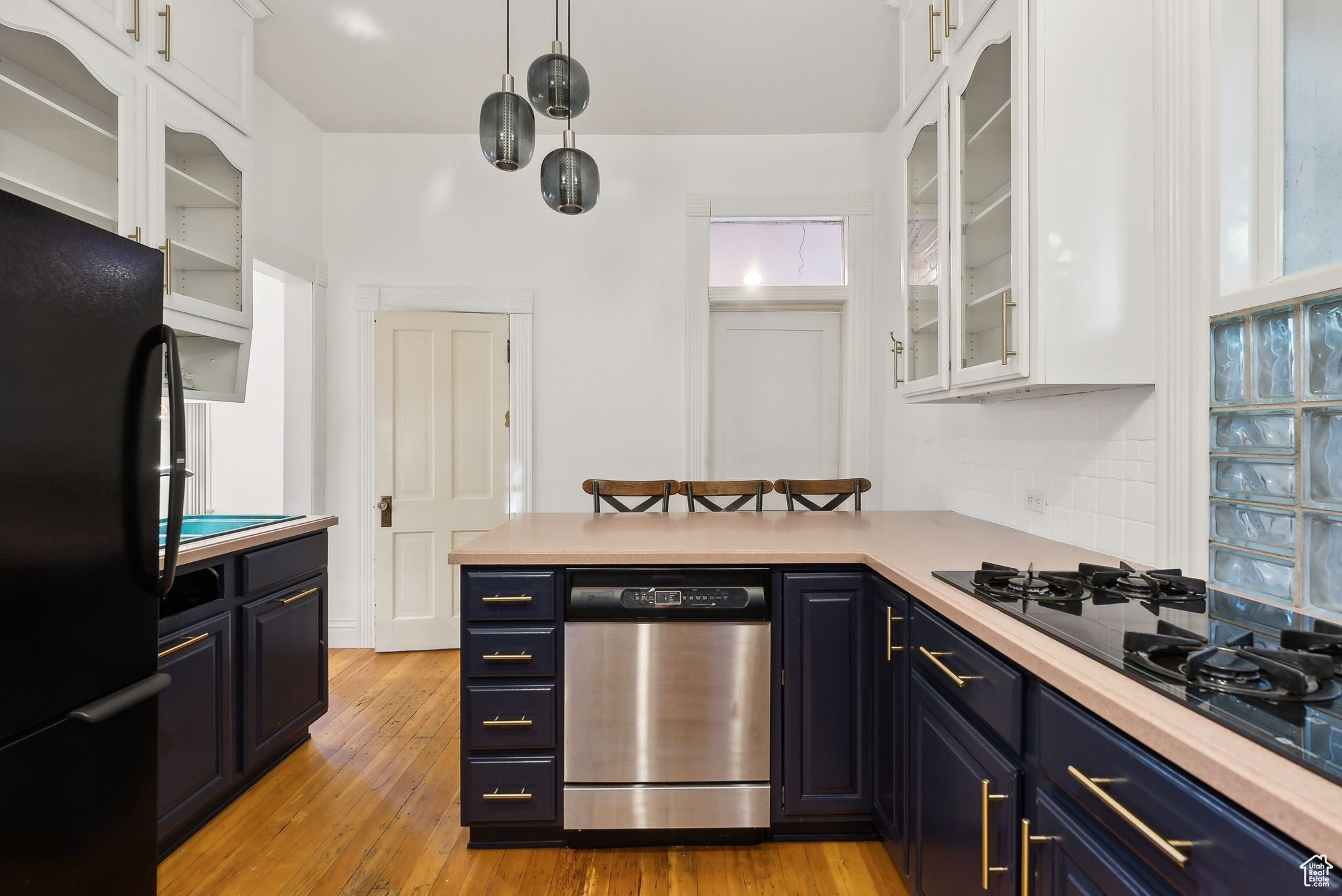 Kitchen with white cabinets, black appliances, light hardwood / wood-style flooring, blue cabinetry, and decorative light fixtures