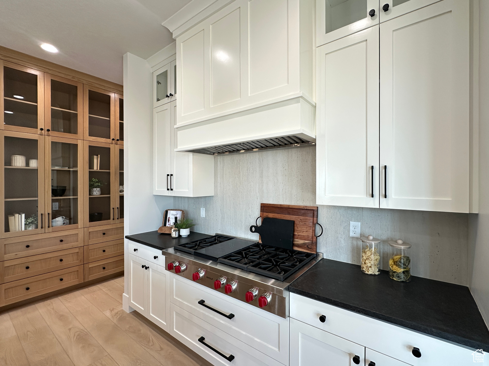 Kitchen with custom exhaust hood, backsplash, white cabinets, light hardwood / wood-style flooring, and stainless steel gas cooktop