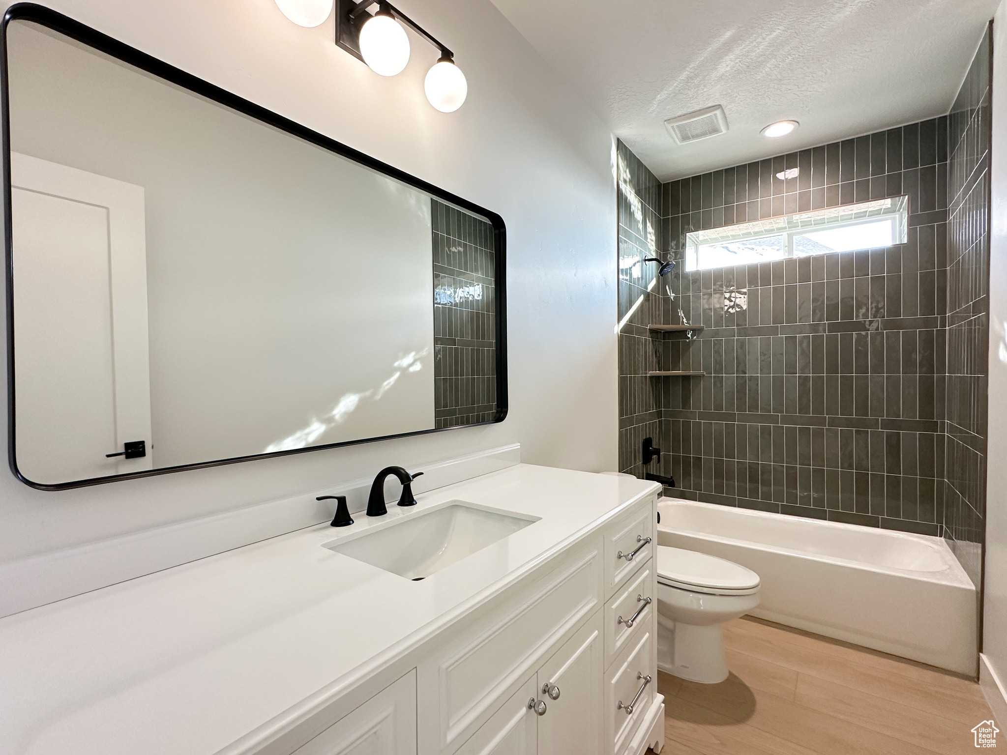 Full bathroom with tiled shower / bath combo, wood-type flooring, a textured ceiling, toilet, and vanity