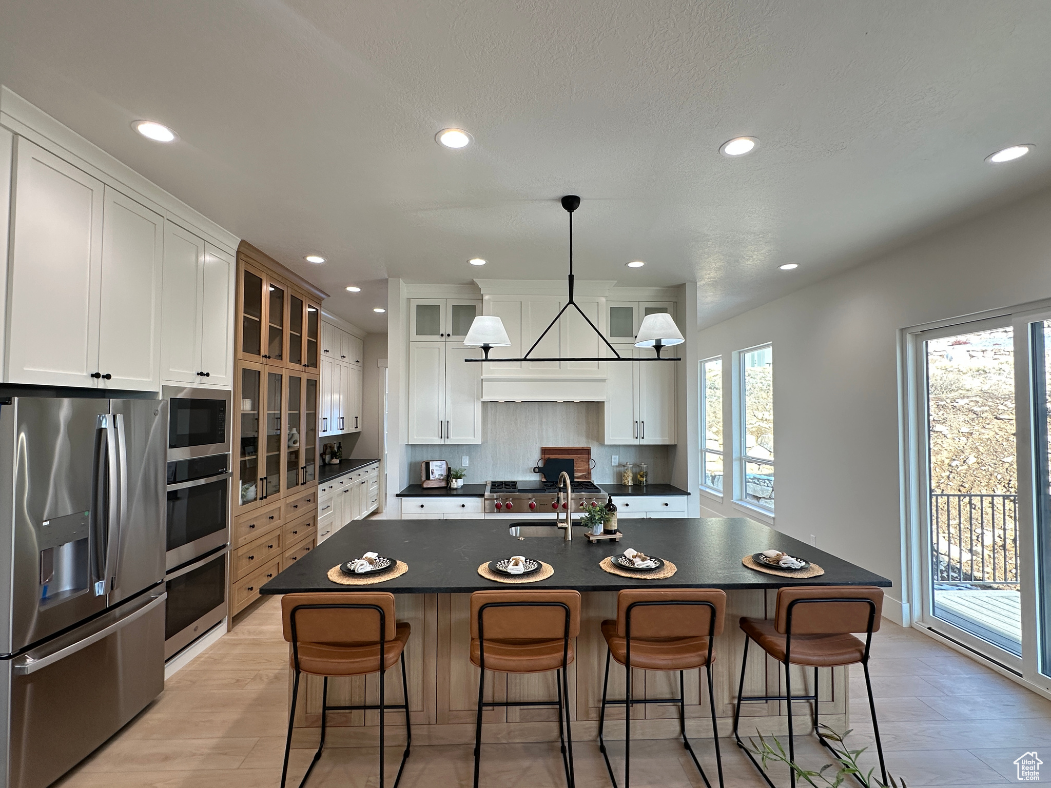 Kitchen featuring white cabinets, decorative light fixtures, stainless steel appliances, and an island with sink