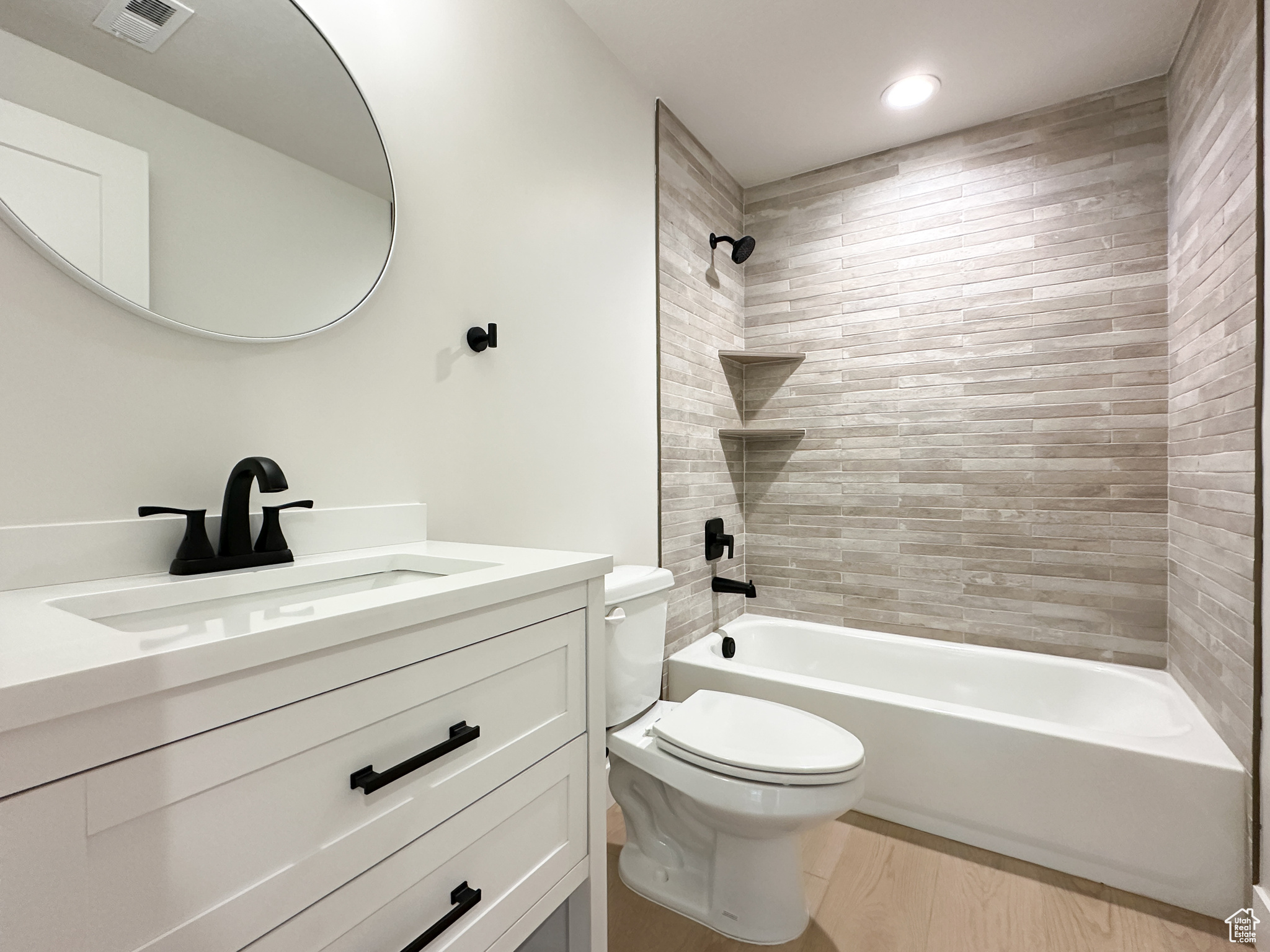 Full bathroom with hardwood / wood-style floors, vanity, tiled shower / bath combo, and toilet