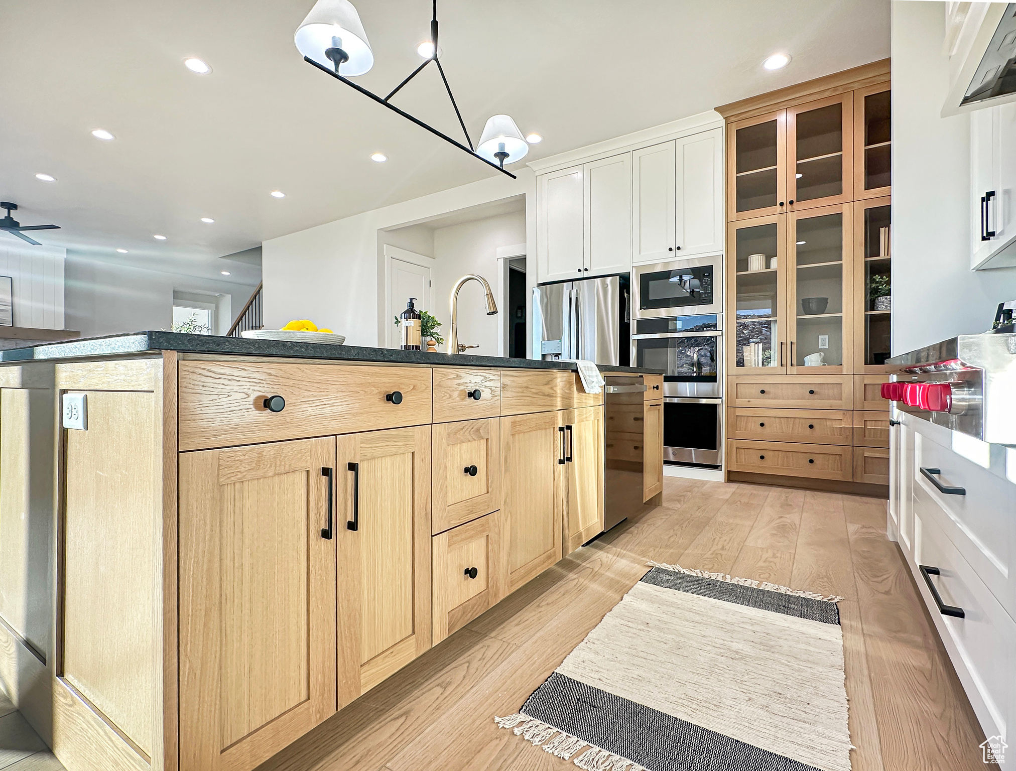 Kitchen featuring light brown cabinets, a kitchen island with sink, ceiling fan with notable chandelier, appliances with stainless steel finishes, and light hardwood / wood-style floors