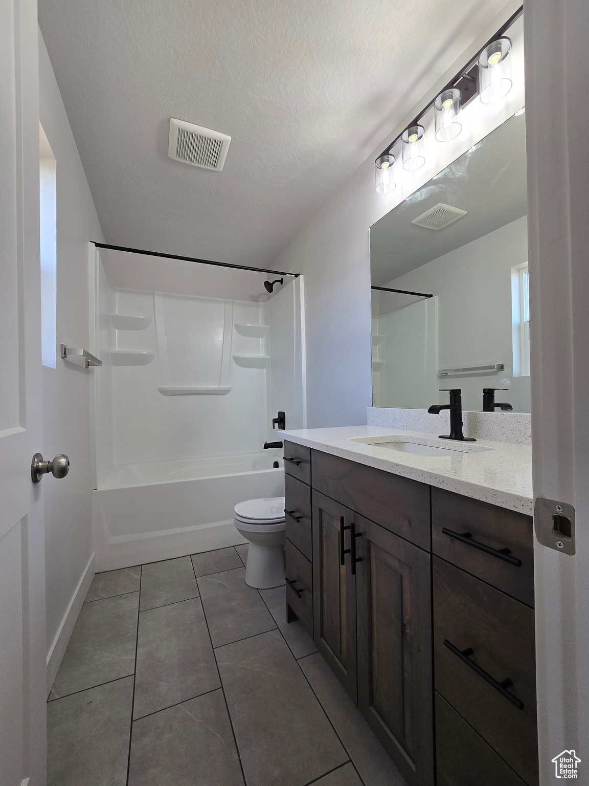 Full bathroom with tile patterned floors, vanity, a textured ceiling,  shower combination, and toilet