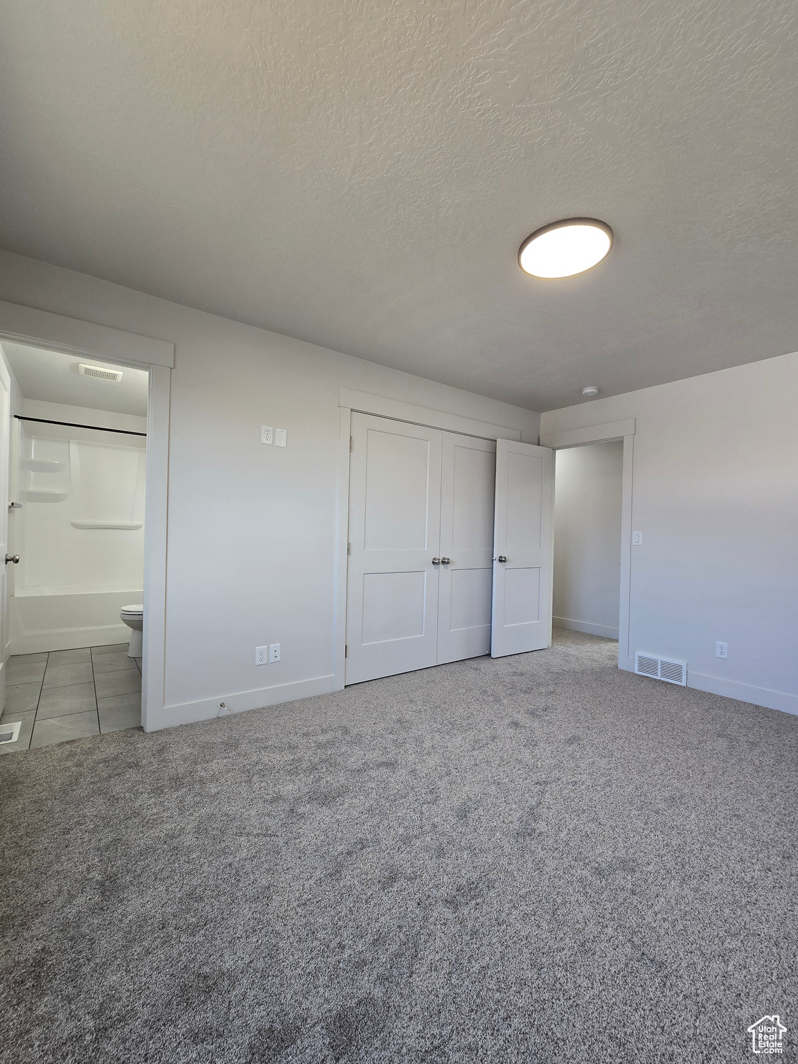 Unfurnished bedroom with carpet flooring, a textured ceiling, and connected bathroom