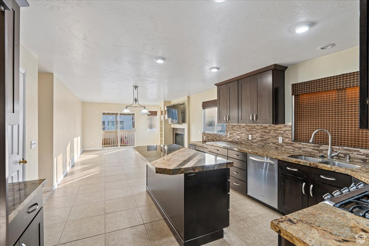 Kitchen featuring backsplash, stainless steel dishwasher, dark brown cabinetry, sink, and a center island