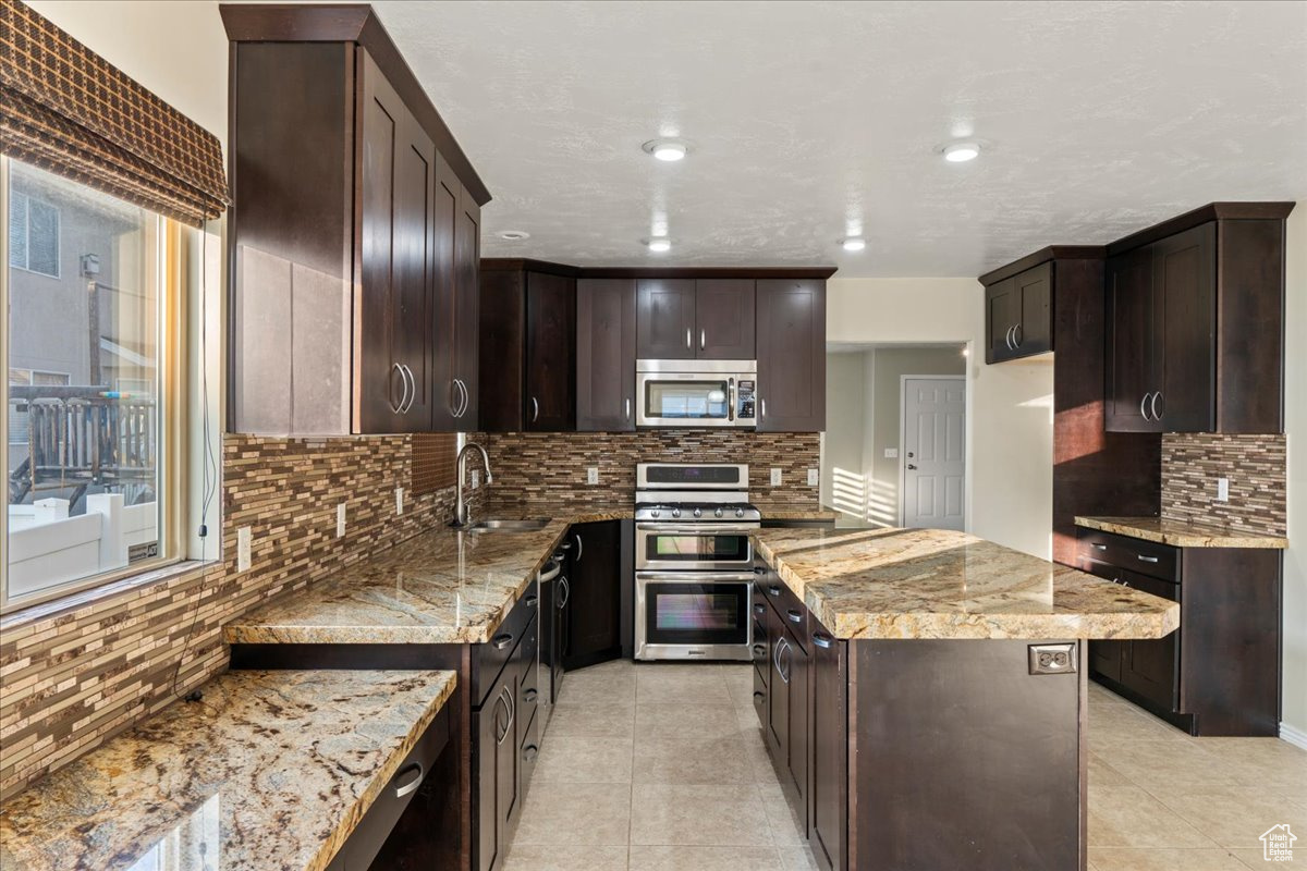 Kitchen with sink, light stone countertops, appliances with stainless steel finishes, tasteful backsplash, and dark brown cabinets