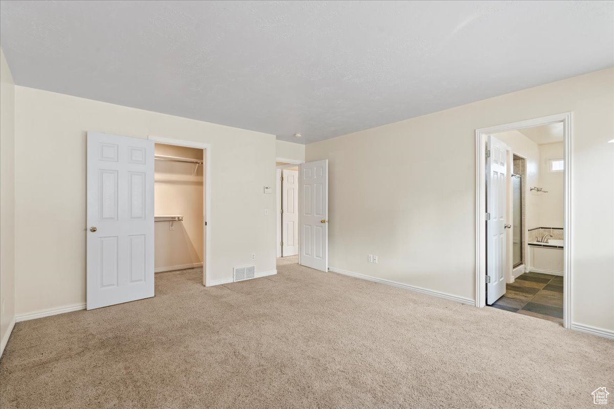 Unfurnished bedroom with connected bathroom, a walk in closet, a closet, and carpet