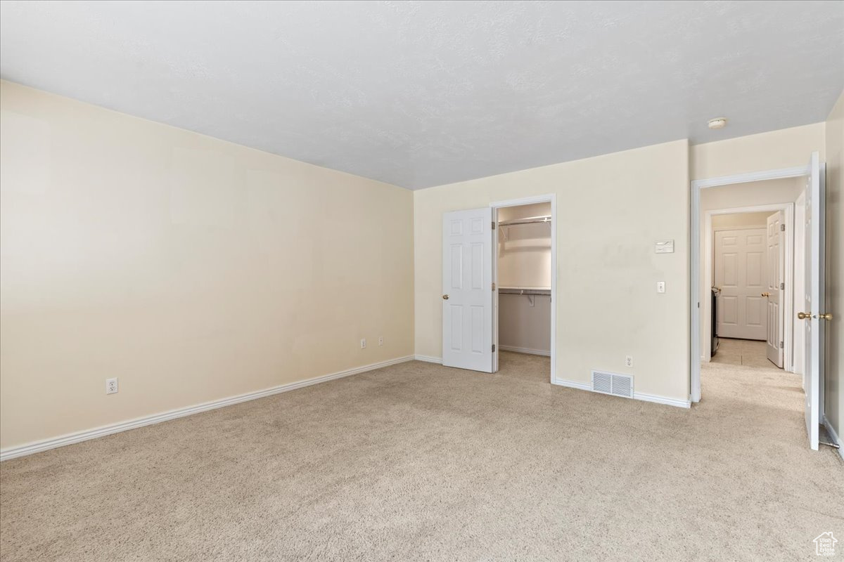 Unfurnished bedroom with light carpet, a closet, and a spacious closet