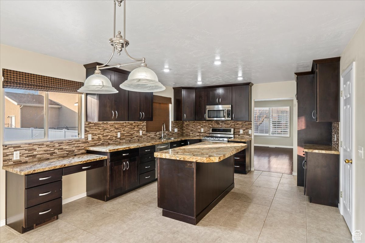 Kitchen with backsplash, appliances with stainless steel finishes, decorative light fixtures, a kitchen island, and dark brown cabinetry