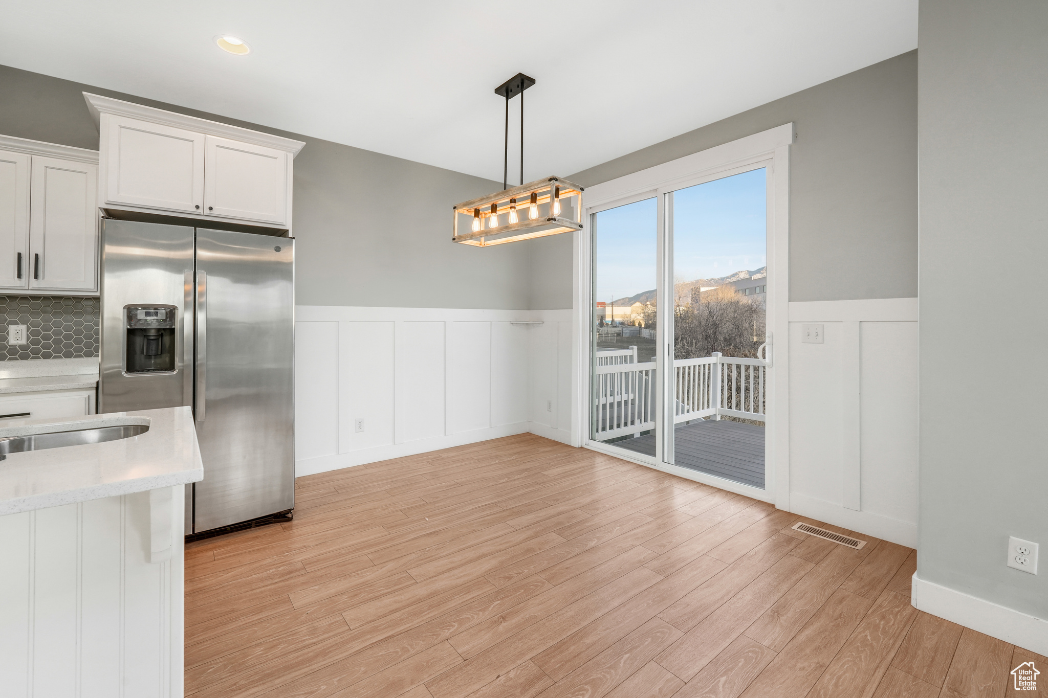 Kitchen with tasteful backsplash, stainless steel refrigerator with ice dispenser, pendant lighting, white cabinets, and light wood-type flooring