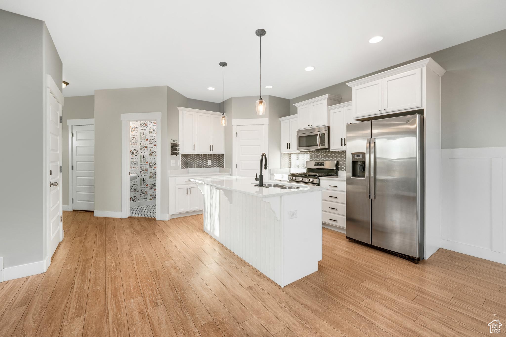 Kitchen featuring appliances with stainless steel finishes, light wood-type flooring, decorative light fixtures, and sink