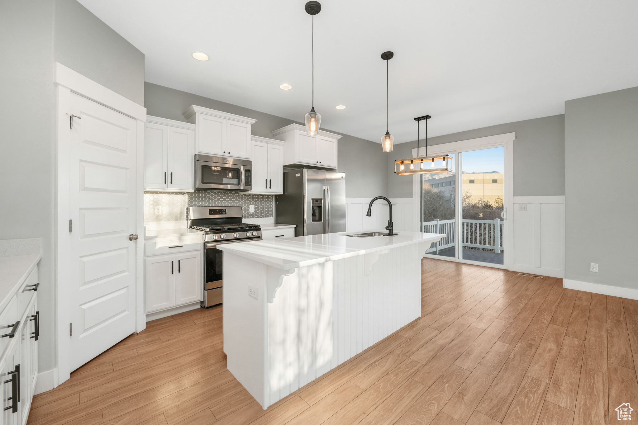 Kitchen with a kitchen island with sink, white cabinets, light hardwood / wood-style floors, and appliances with stainless steel finishes