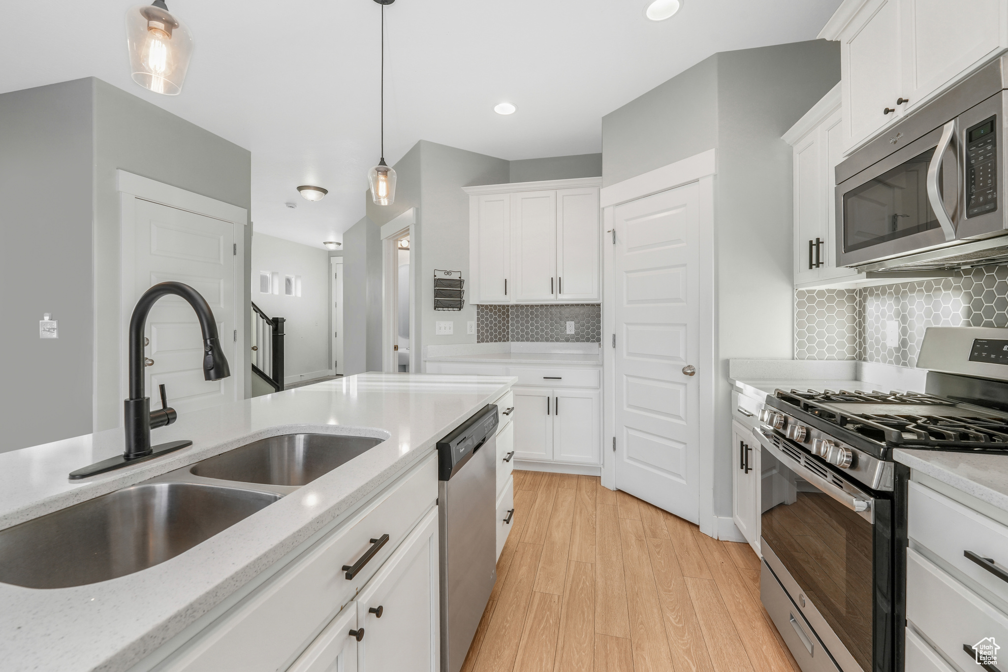 Kitchen with white cabinets, appliances with stainless steel finishes, light wood-type flooring, and tasteful backsplash