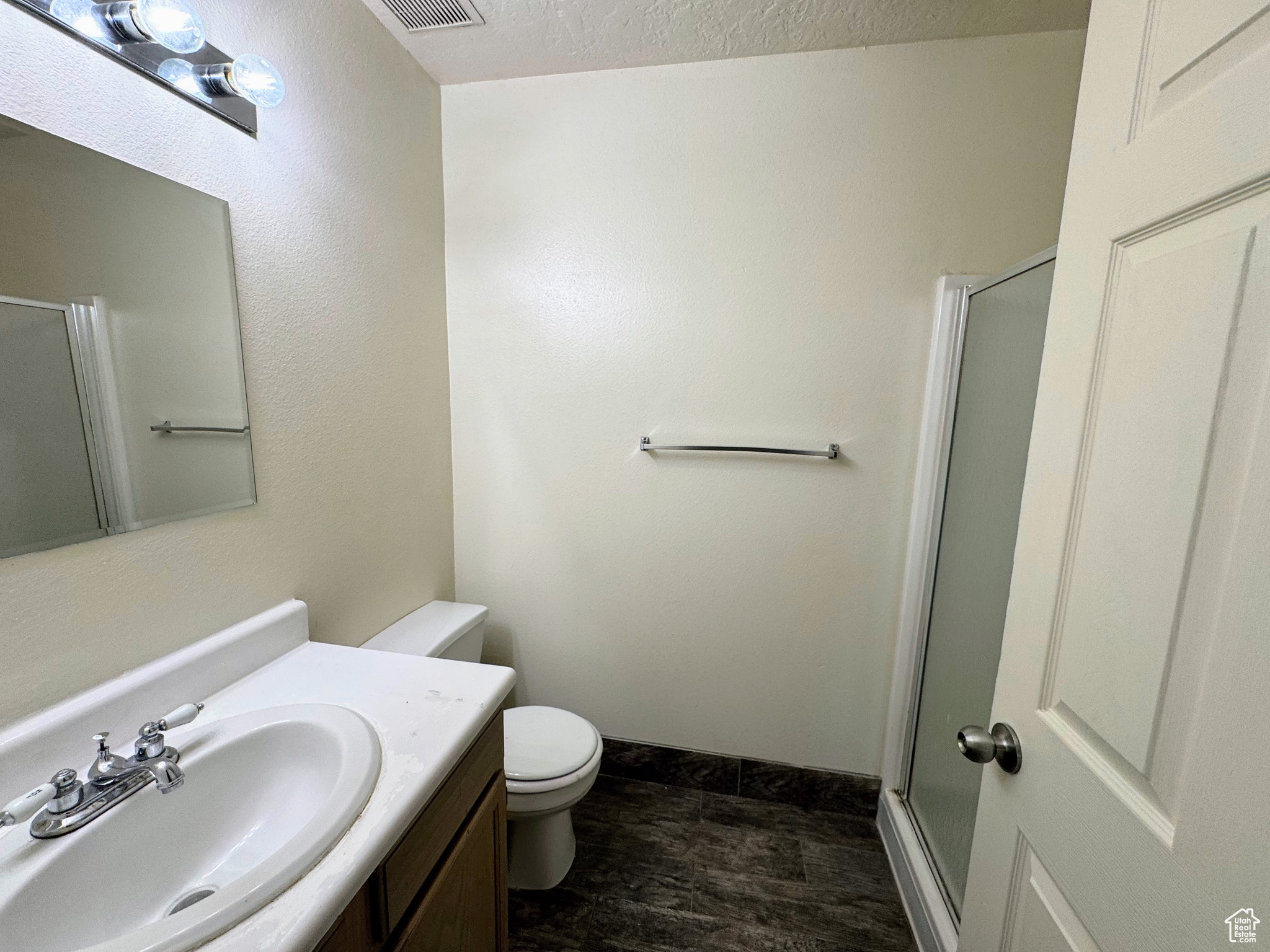 Bathroom with vanity, a shower with shower door, a textured ceiling, and toilet