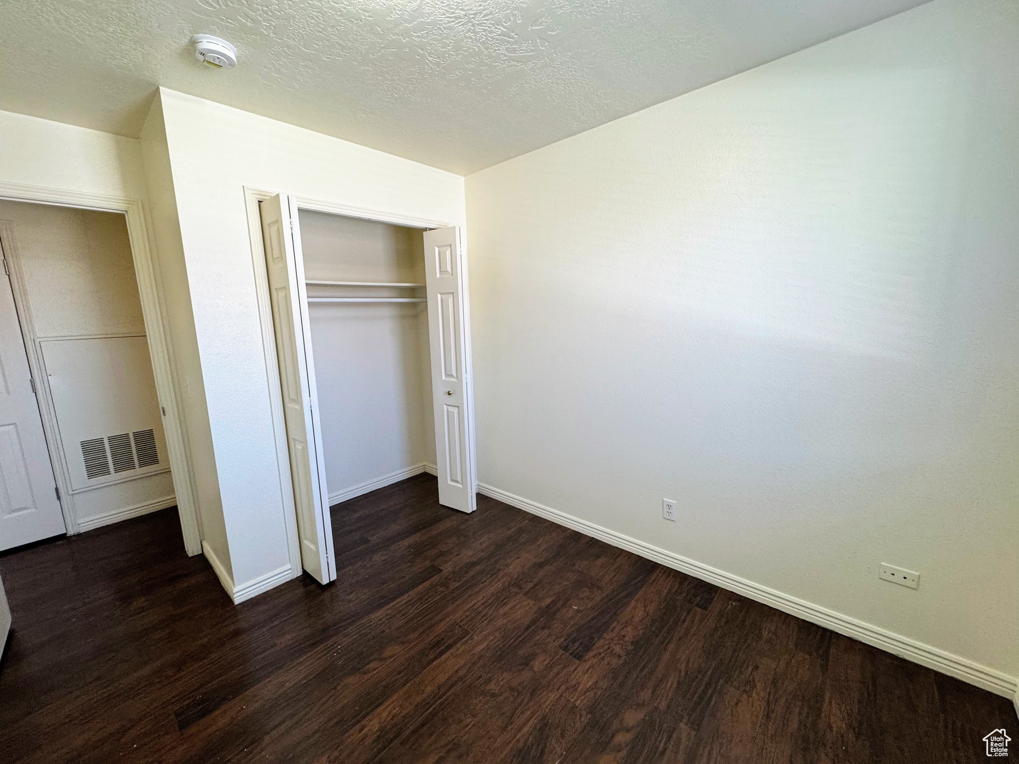 Unfurnished bedroom featuring dark hardwood / wood-style flooring, a textured ceiling, and a closet