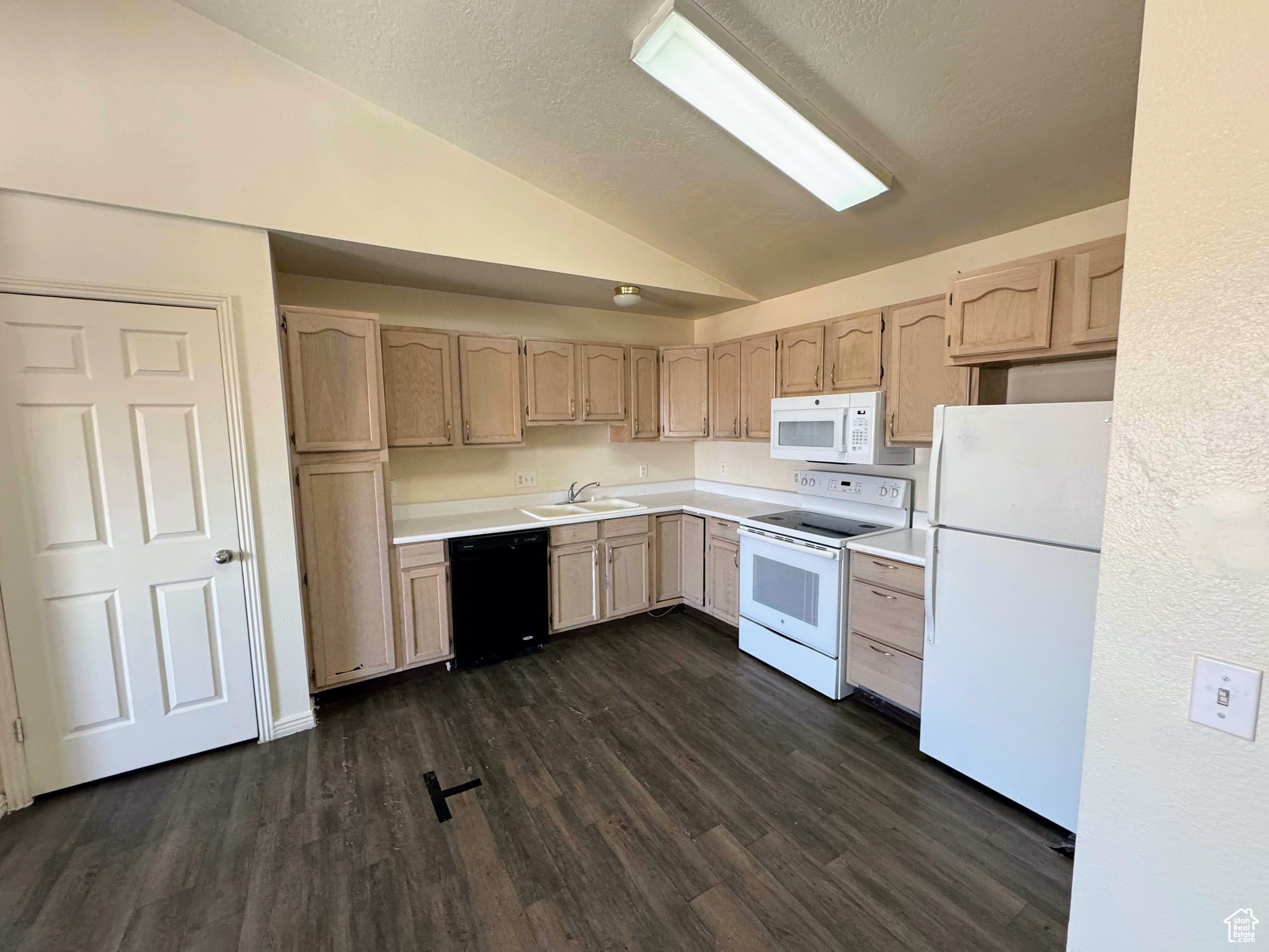 Kitchen with light brown cabinets, sink, dark hardwood / wood-style flooring, vaulted ceiling, and white appliances