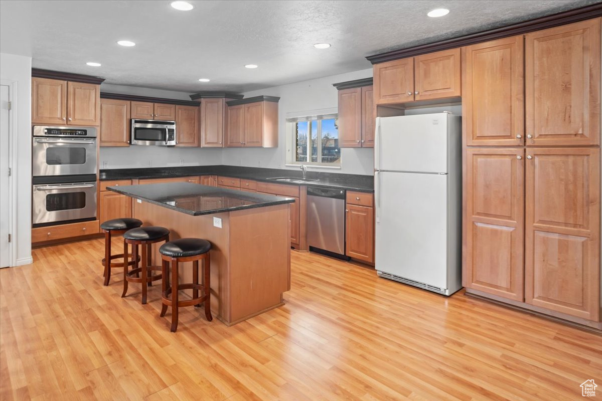 Kitchen with granite countertops, stainless steel appliances, light hardwood / wood-style floors, and a kitchen island