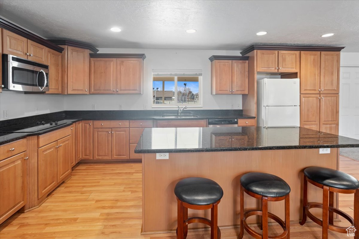 Kitchen with granite countertops, stainless steel appliances, light hardwood / wood-style floors, and a kitchen island