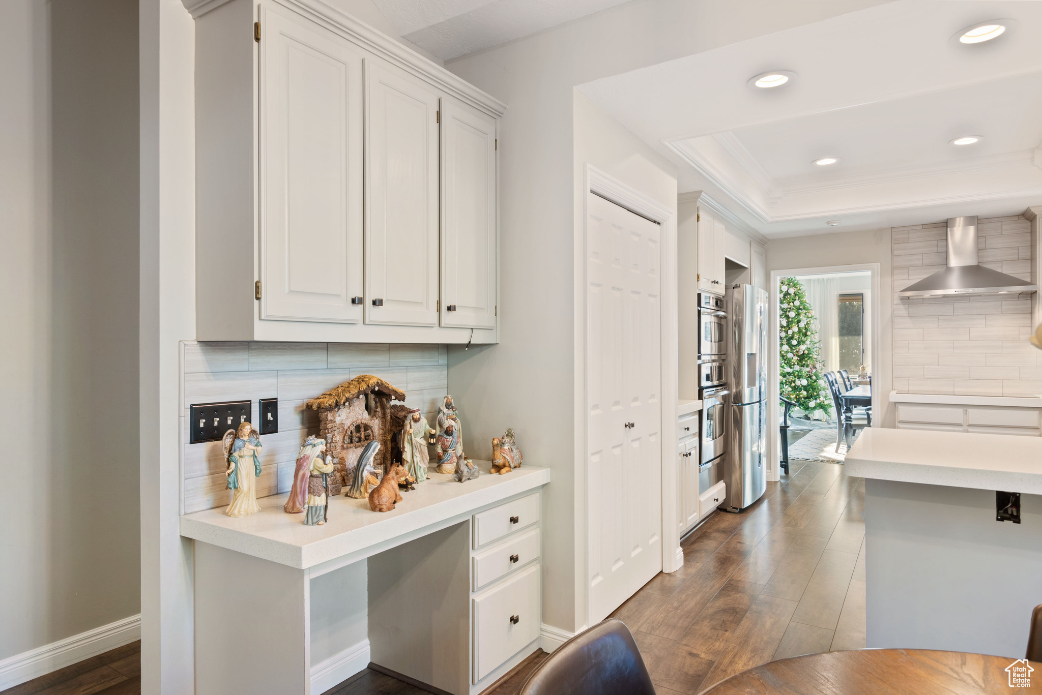 Kitchen with backsplash, a raised ceiling, wall chimney range hood, dark hardwood / wood-style flooring, and white cabinetry