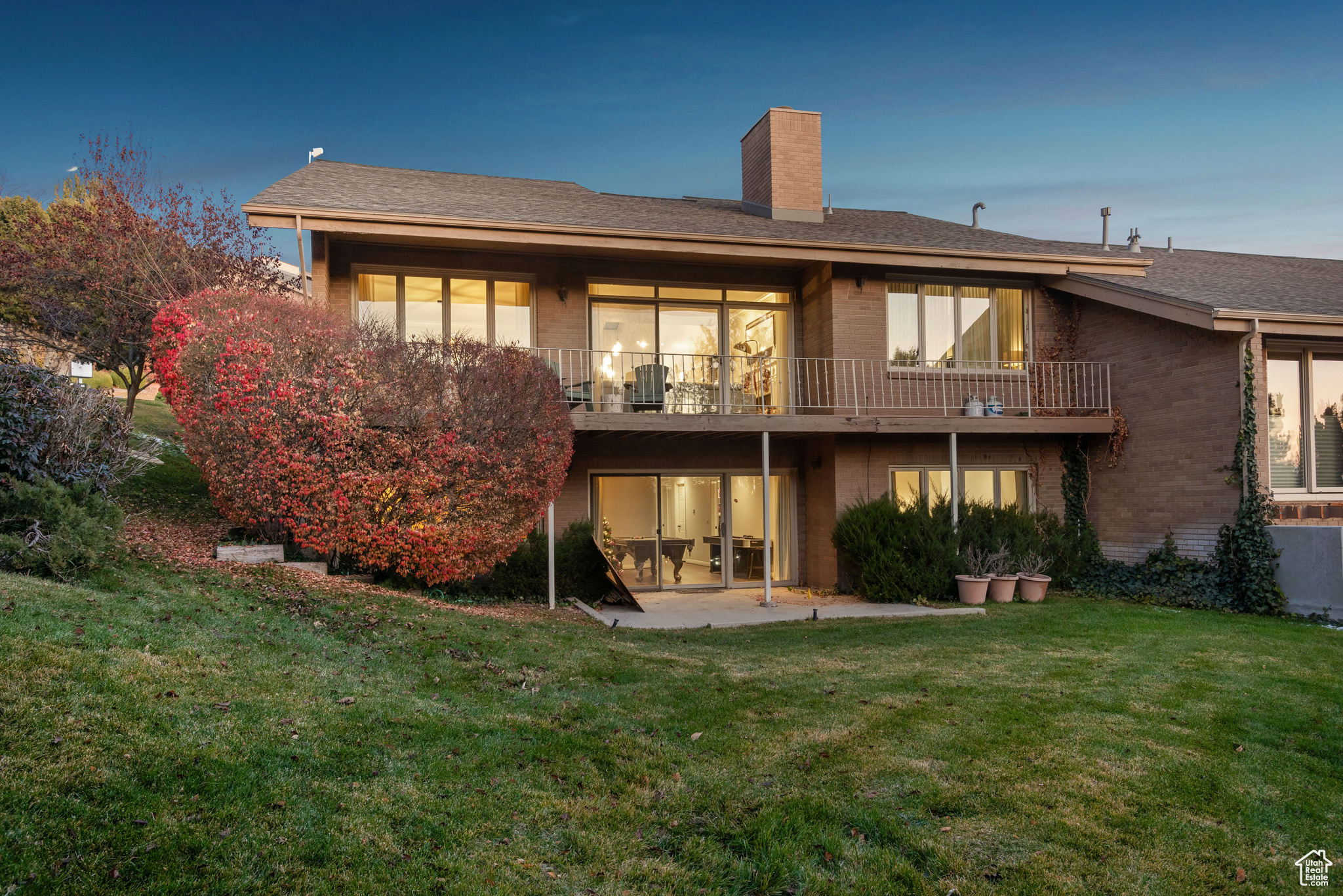 Back house at dusk featuring a balcony, a yard, and a patio