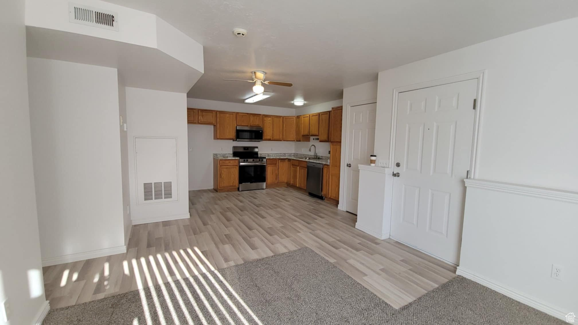 Kitchen with appliances with stainless steel finishes, light hardwood / wood-style flooring, ceiling fan, and sink