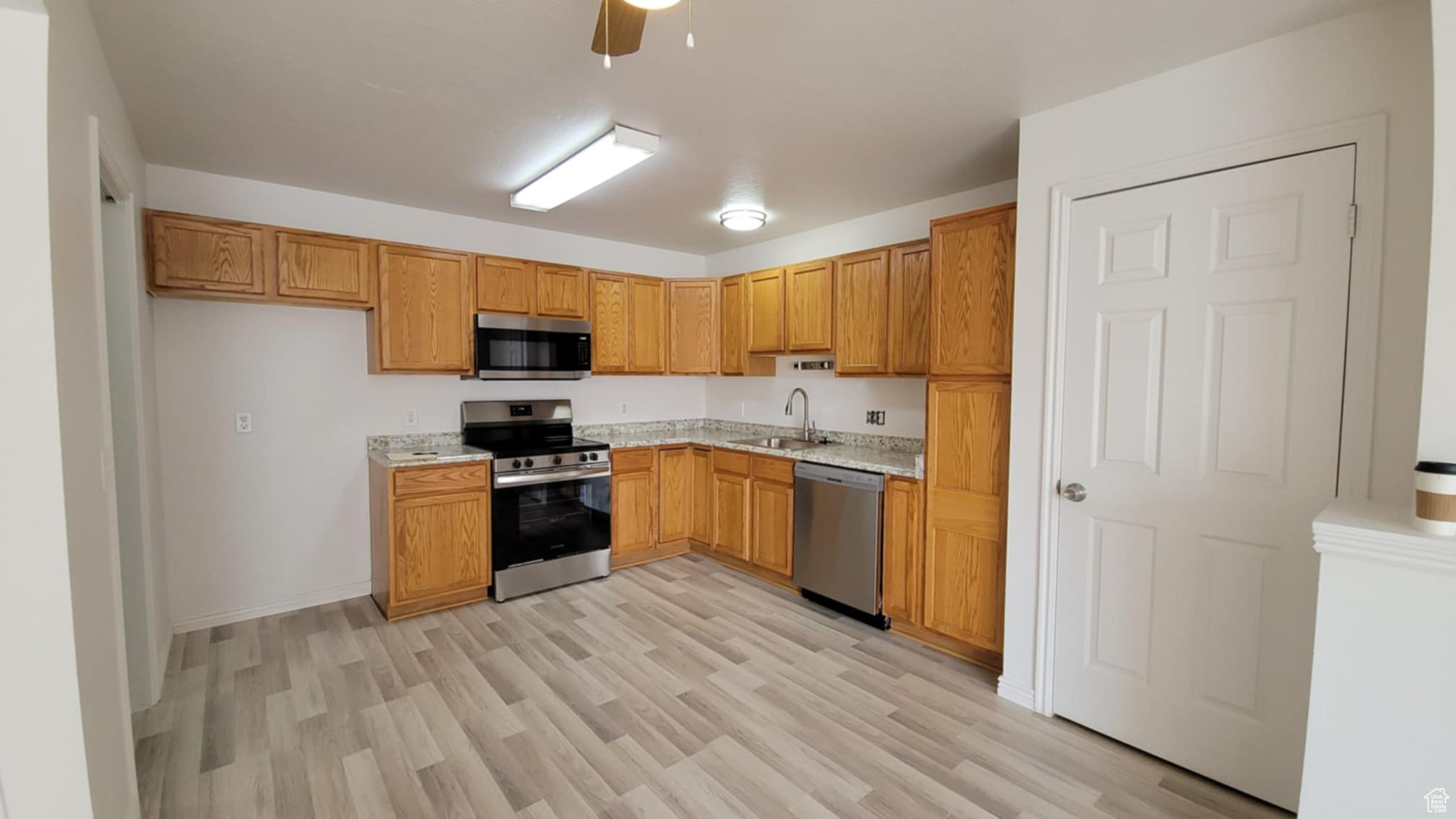 Kitchen featuring light stone counters, stainless steel appliances, ceiling fan, sink, and light hardwood / wood-style floors