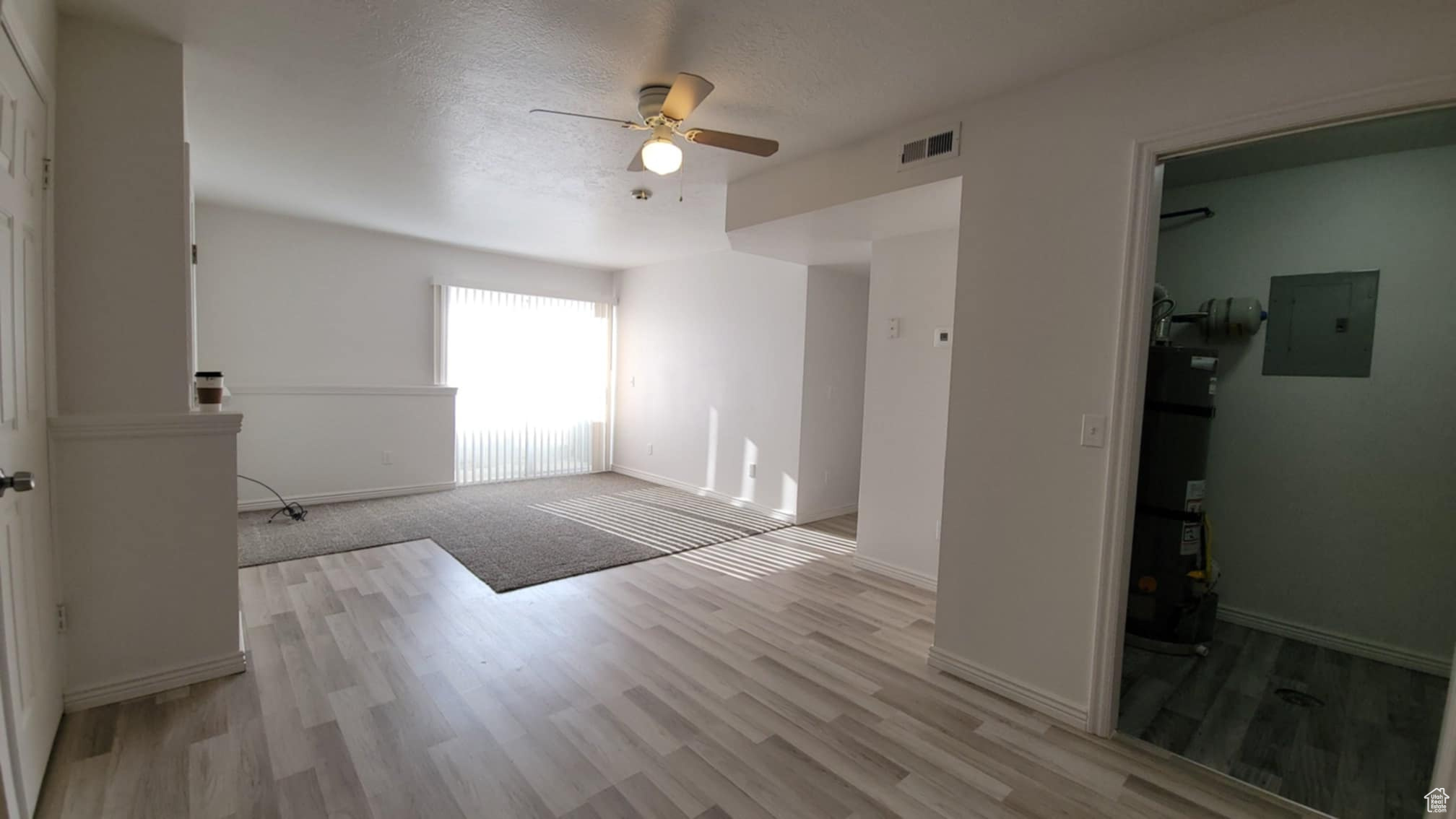 Interior space featuring ceiling fan, strapped water heater, electric panel, and light hardwood / wood-style flooring