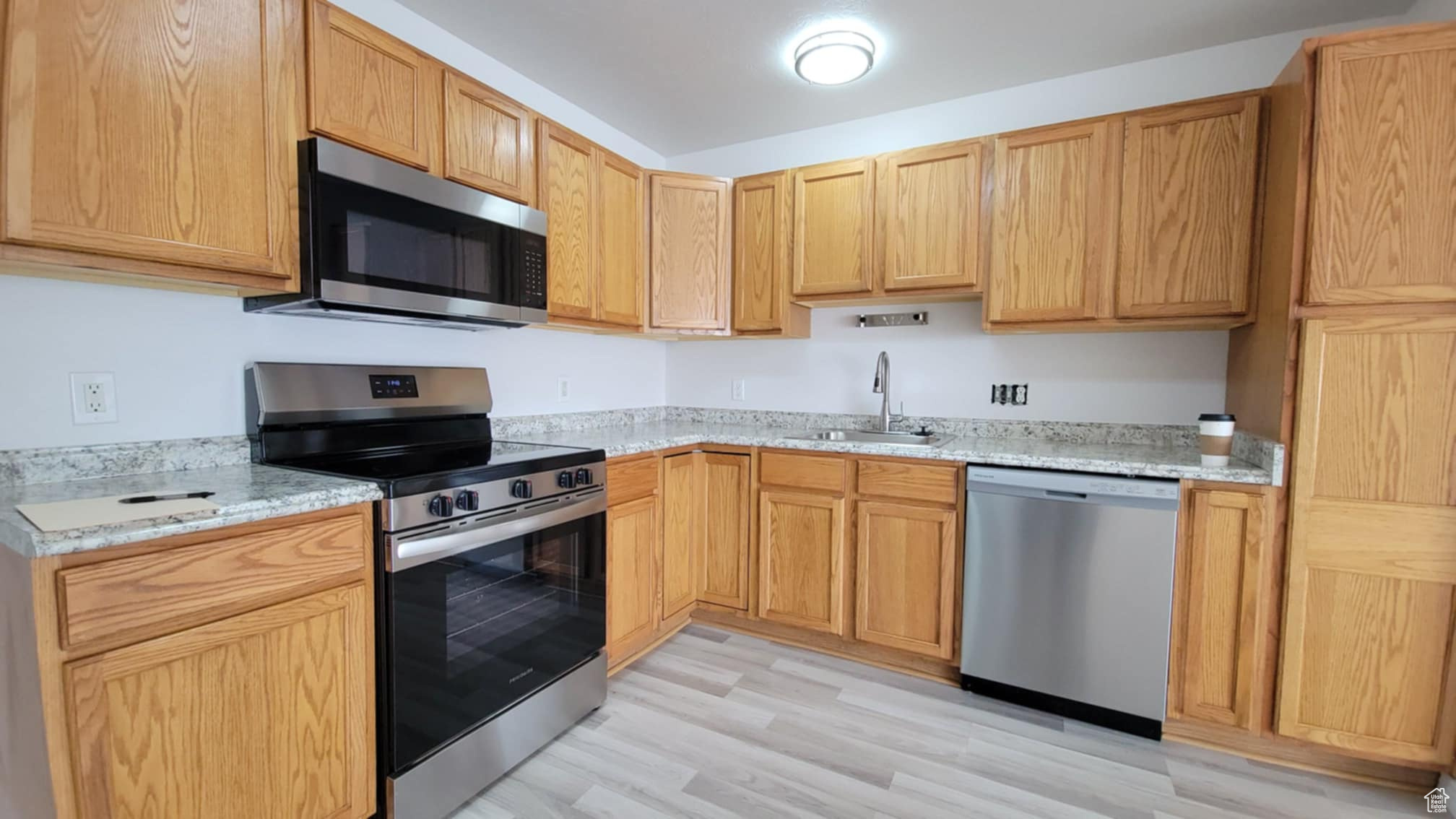 Kitchen with light stone countertops, sink, light hardwood / wood-style floors, and appliances with stainless steel finishes