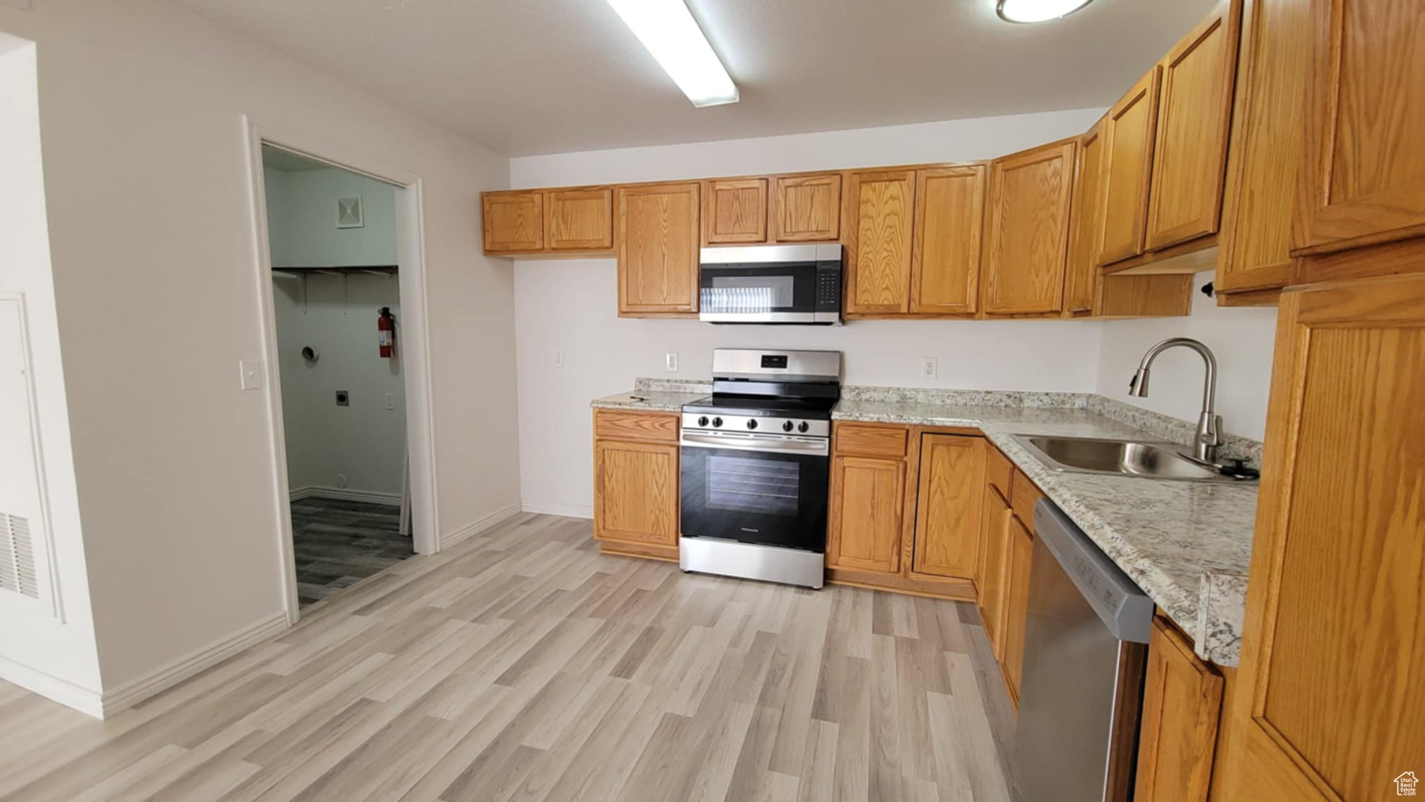 Kitchen featuring light stone countertops, appliances with stainless steel finishes, light hardwood / wood-style floors, and sink