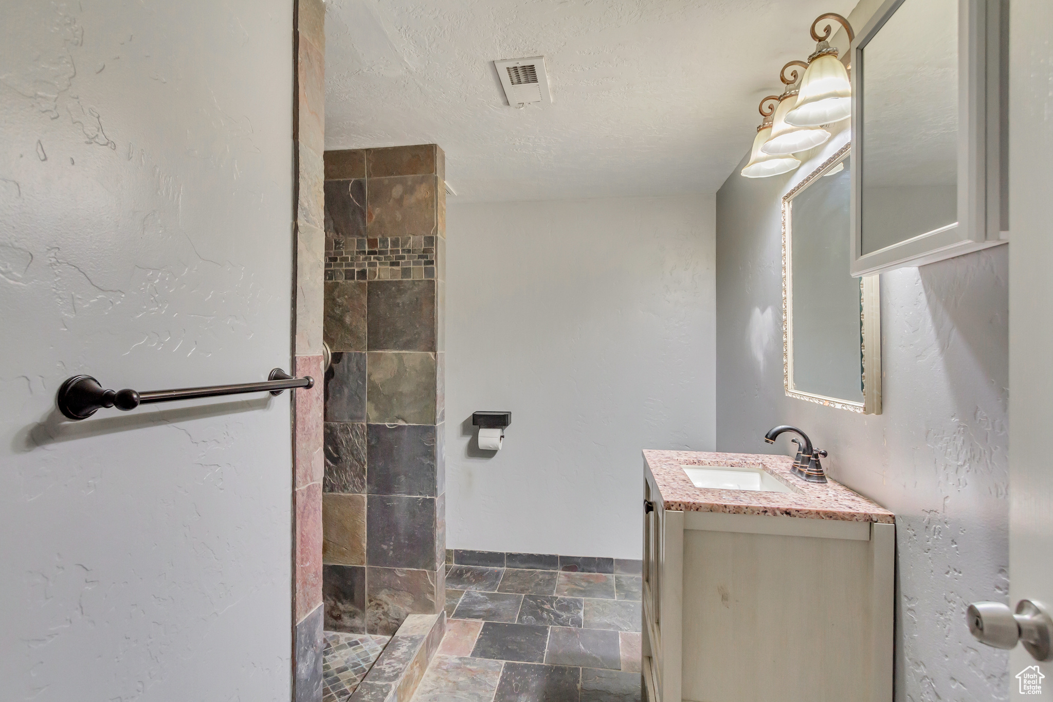 Bathroom with vanity, a textured ceiling, and tiled shower