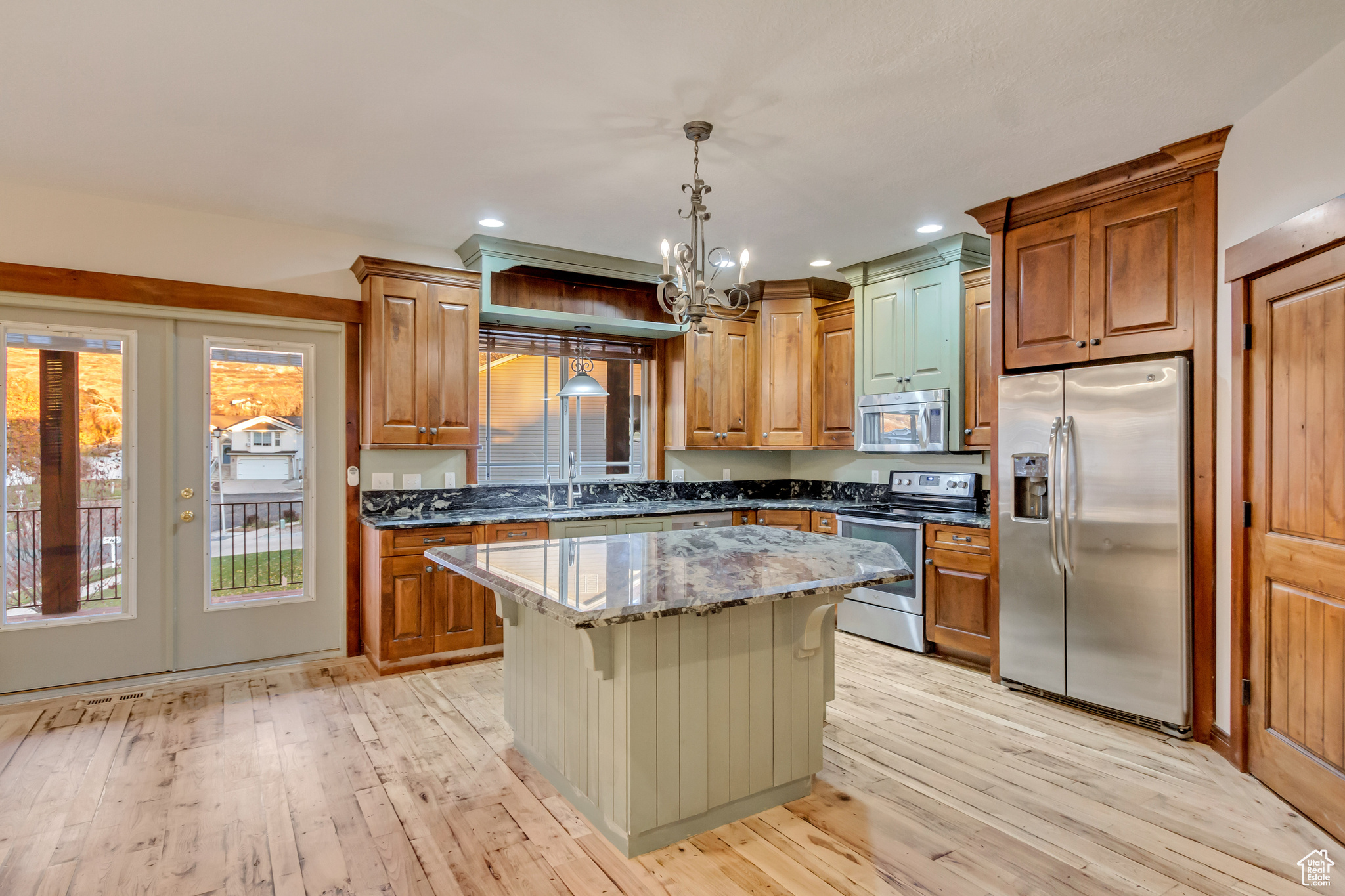 Kitchen featuring dark stone counters, hanging light fixtures, light hardwood / wood-style floors, appliances with stainless steel finishes, and a kitchen island