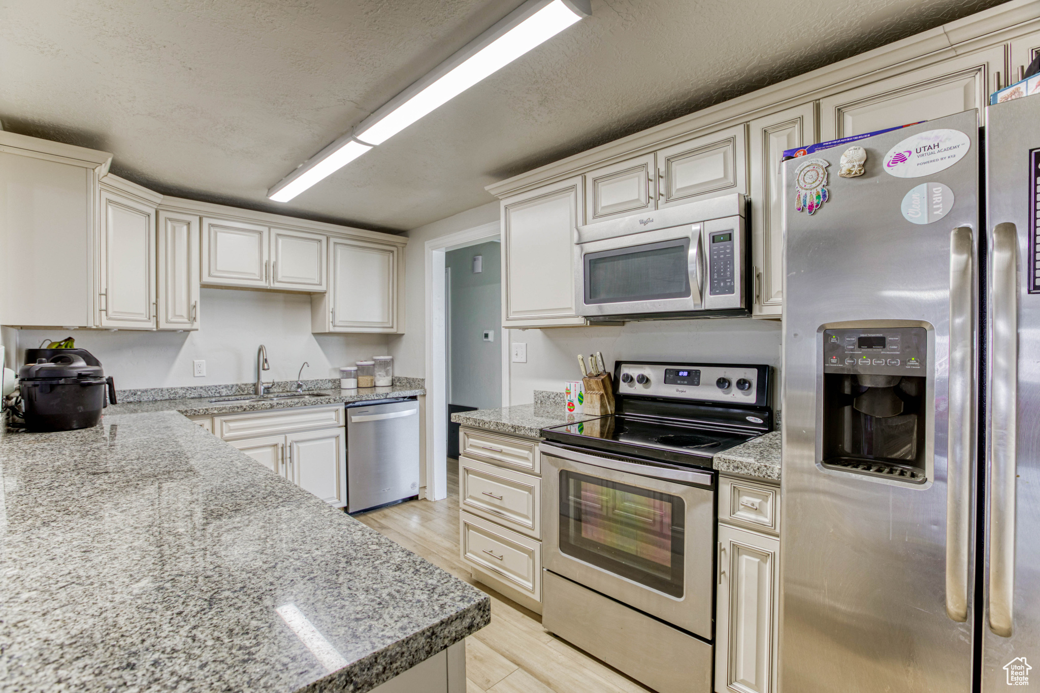 Kitchen featuring sink, light wood-type flooring, a textured ceiling, light stone counters, and stainless steel appliances